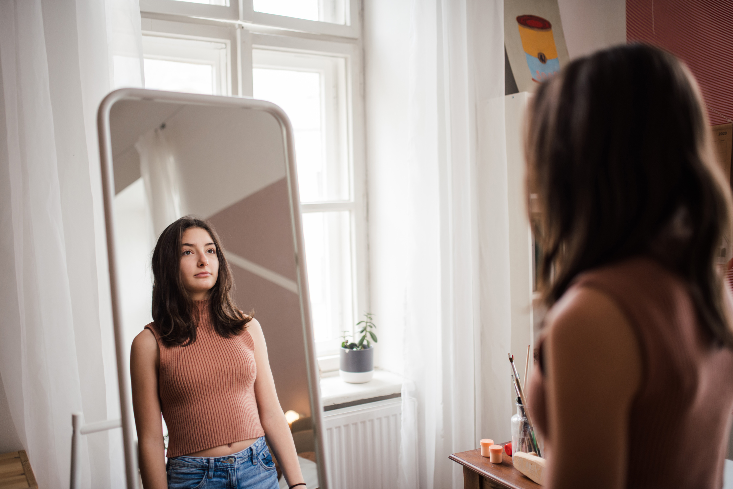 Young Teenage Girl Looking in the Mirror in Her Room.